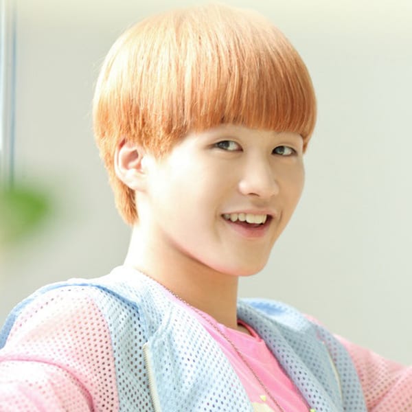Bokeun has red (orange) hair. He is wearing a baby blue holed jacket, with baby pink sleeves, over a neon pink shirt