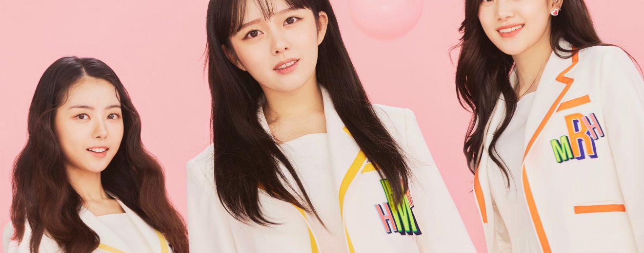 The female members of the group TEAPARTY alongside a pink background. They wear bright clothing. They are standing in a line facing front. From left to right, its Hyunji, Maha and then Ria. Above the members, there is the group logo ‘TEA PARTY’ in a fancy white design. There is also pink bubbles all around the members.