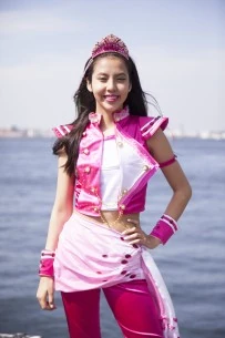 Shiori posing with her left hand on her hip in front of the ocean. she is wearing a pink outfit.